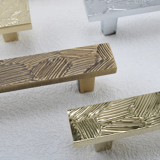 detailfoto van langwerpige vlakke meubelgrepen met abstract geometrisch patroon in goud, chroom en brons
