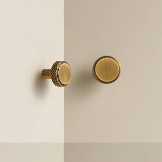 Ronde platte meubelknop op een slank staafvormig voetje knurled effect op de zijkant en uitgevoerd in brons op een witte kast