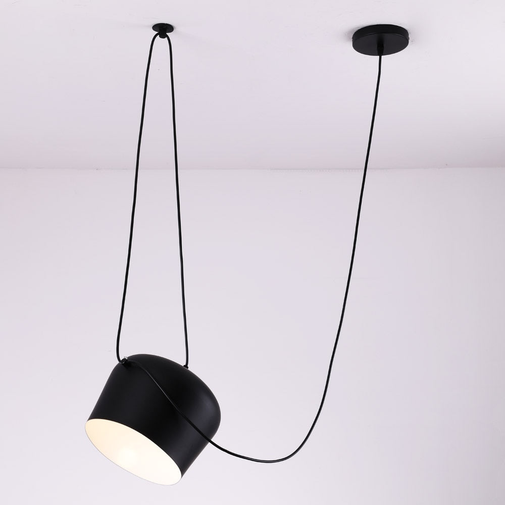 enkele industriële zwarte hanglamp met een zwart snoer aan een wit plafond tegen een witte muur