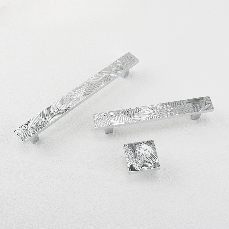 overzicht van rechthoekige meubelgrepen en vierkante meubelknop  met een abstract geometrisch patroon uitgevoerd in chroom.