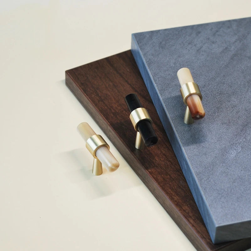 drie T-model meubelknopjes mat messing met hoorn op een ondergrond van beige blauw en hout