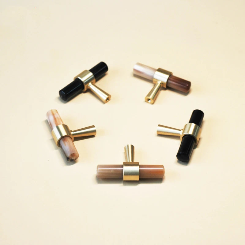 vijf t-model meubelknopjes mat messing en wit en zwart hoorn liggend  in een cirkel op een beige tafel 