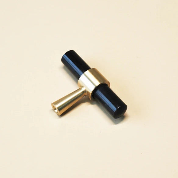 t-model meubelknopje mat messing en zwart liggend op een beige ondergrond