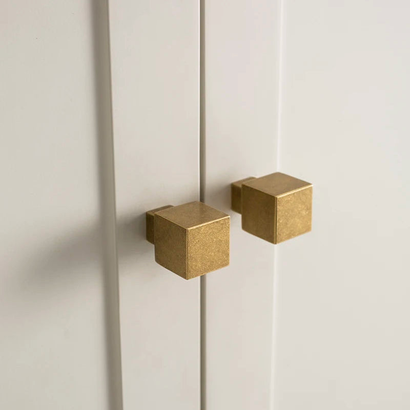 twee vierkante antiek messing meubelknopjes op een witte kast