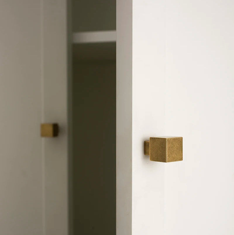 twee vierkante antiek messing meubelknopjes op een witte kast, 1 knopje wazig in de achtergrond 