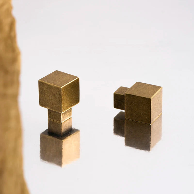 2 vierkante antiek messing meubelknopjes op een spiegel ondergrond