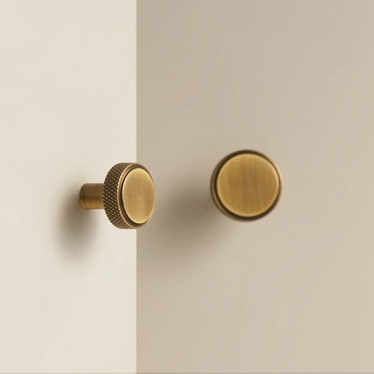 2 ronde brons kleurige meubelknopjes met een knurled rand op een witte kast