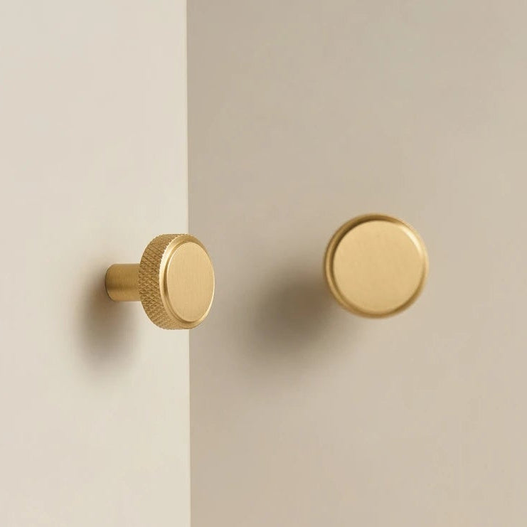 2 ronde meubelknopjes in mat messing met knurled rand op een witte kast
