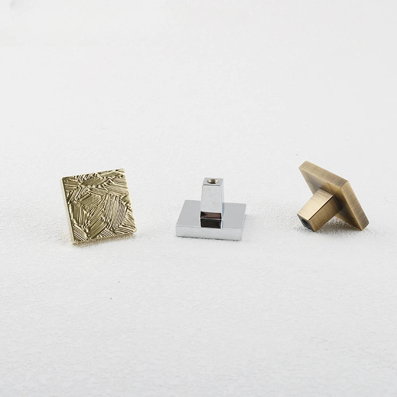 3 vierkante meubelknoppen met abstract geometrisch patroon in goud, chroom en brons 